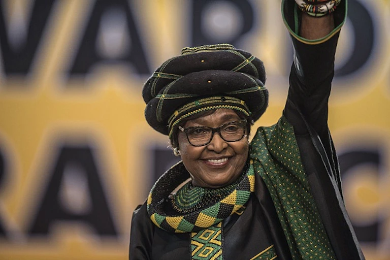 A woman wearing in a turban raises her left hand in a black power salute