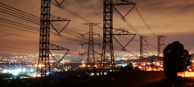 Power lines towering over the lit up city at night time in Johannesburg, South Africa.