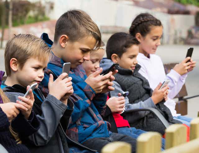 A row of children sit looking at phones