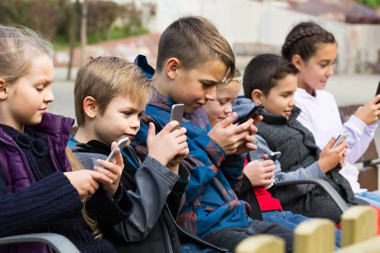 A row of children sit looking at phones