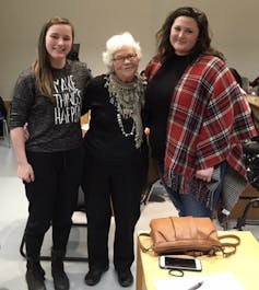 Two younger women stand beside an older woman in the middle.