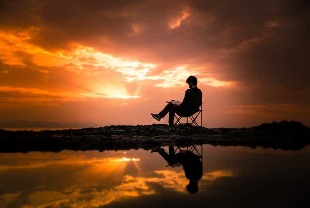 man sits on chair with a sunset 