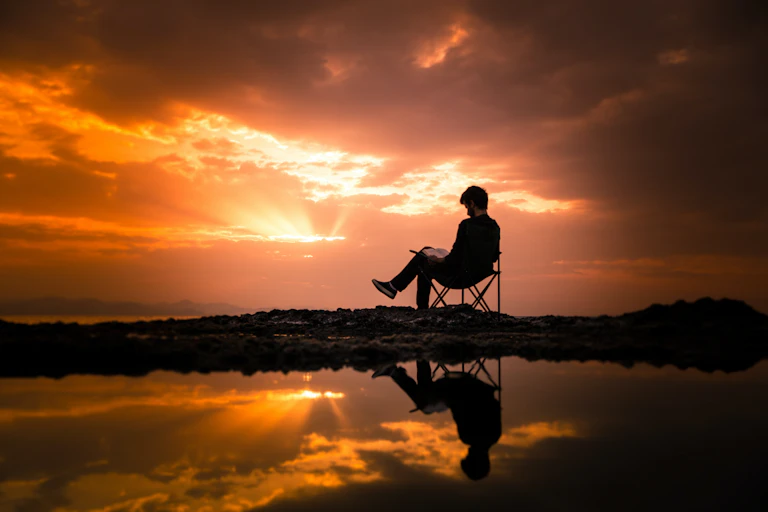man sits on chair with a sunset