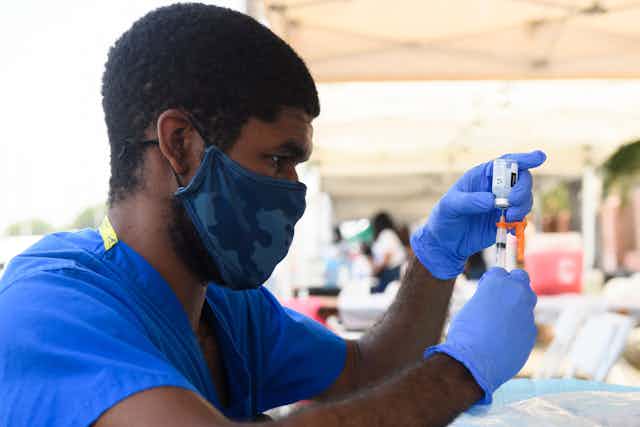 A health care worker wearing a mask and gloves prepares a dose of the Moderna Covid-19 vaccine.