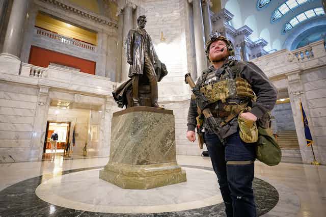 Man carrying gun walks by statue of Abraham Lincoln.