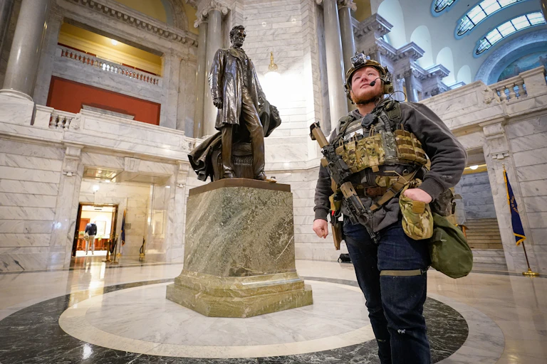Man carrying gun walks by statue of Abraham Lincoln.