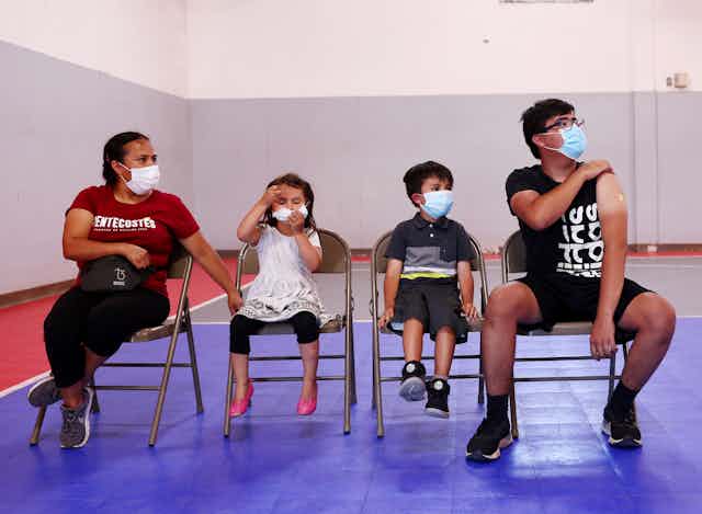 four masked people of different ages seated at a vaccine site