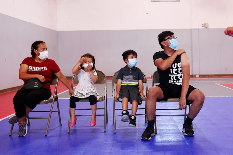 four masked people of different ages seated at a vaccine site