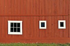 Red side wall of a barn with white framing around windows.