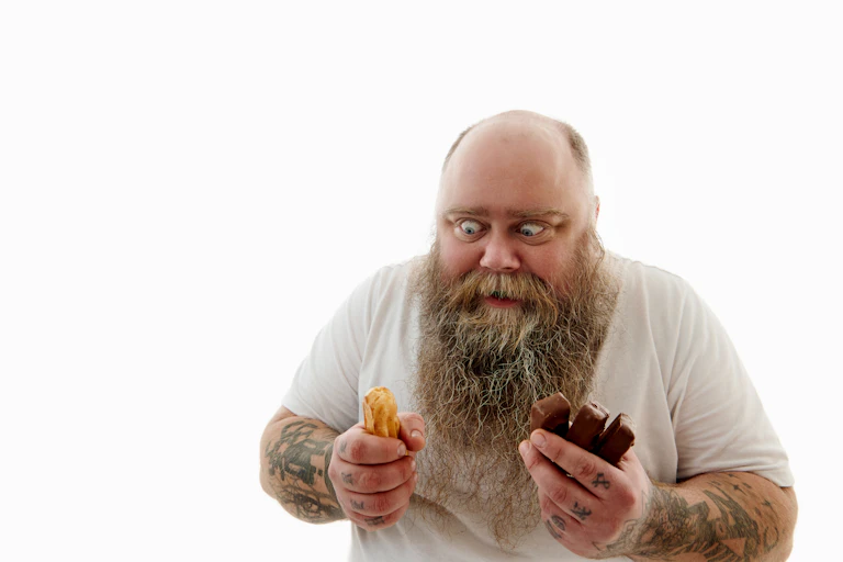 Un homme tient un beignet et du chocolat et les regarde plein d'envie.
