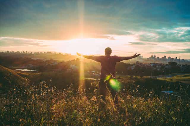 Man standing with open arms at sunrise