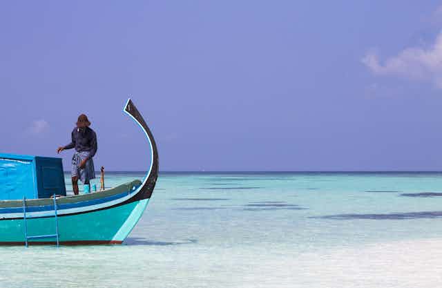 A fisherman in his boat in shallow turquoise water.