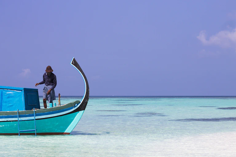 A fisherman in his boat in shallow turquoise water.