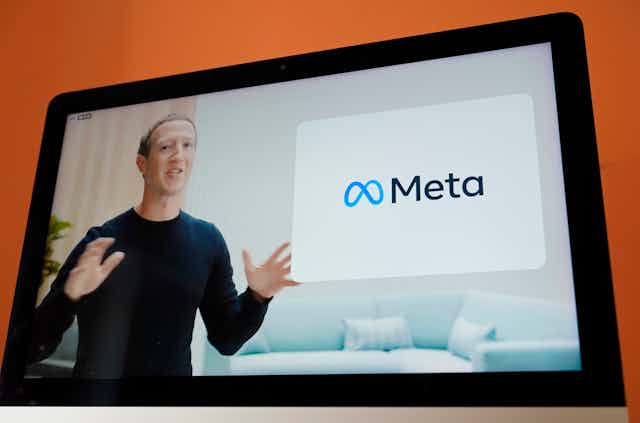 A man on a screen talks in front of a sign that says Meta.