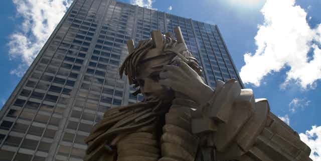 Statue of a stone king seen against a tall skyscraper.