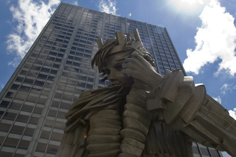 Statue of a stone king seen against a tall skyscraper.