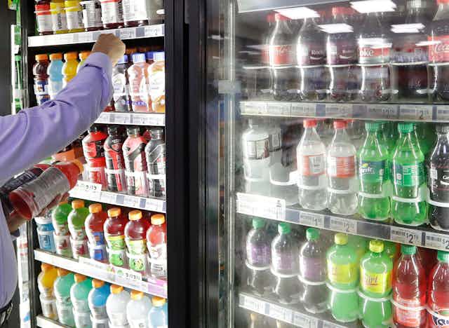 Arm of a man out of shot reaching into a retail refrigerator to choose beverages