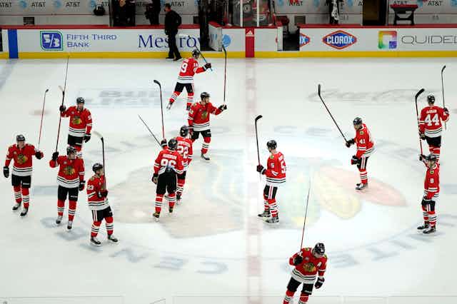 The Chicago Blackhawks skate around centre ice holding their sticks up in the air, celebrating a win