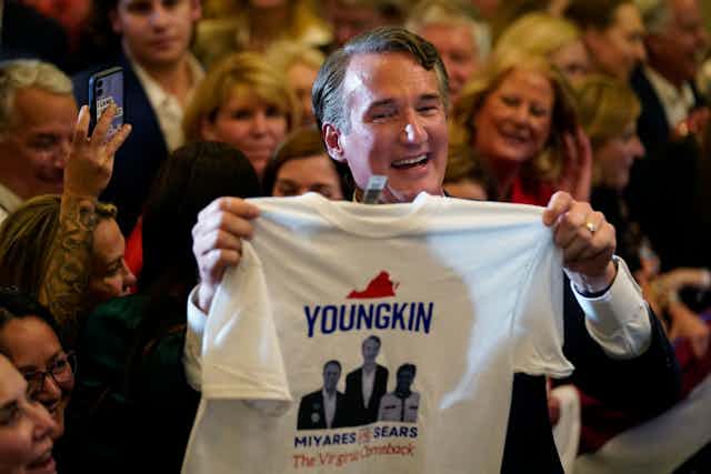 Virginia Gov.-elect Glenn Youngkin greets supporters at an election night party while holding a campaign tshirt.
