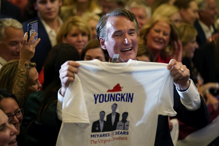 Virginia Gov.-elect Glenn Youngkin greets supporters at an election night party while holding a campaign tshirt.