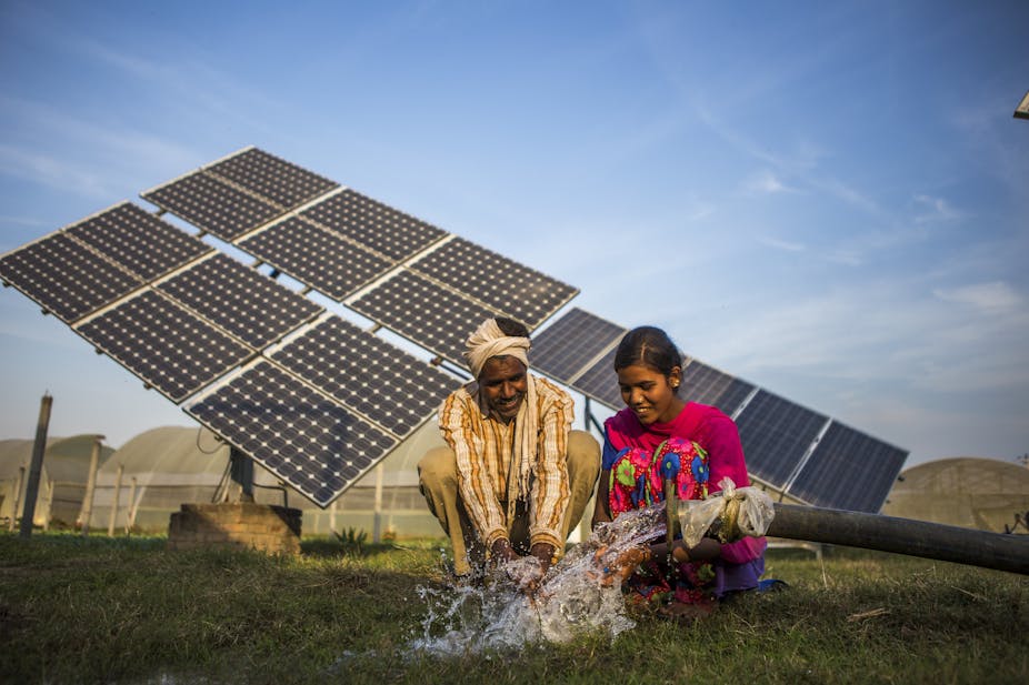 Two people in India sit in front of solar panels