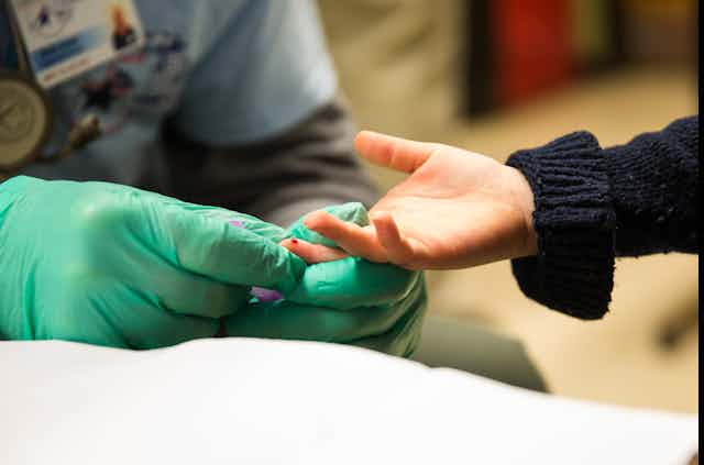A doctor takes a drop of blood from a child's fingertip.