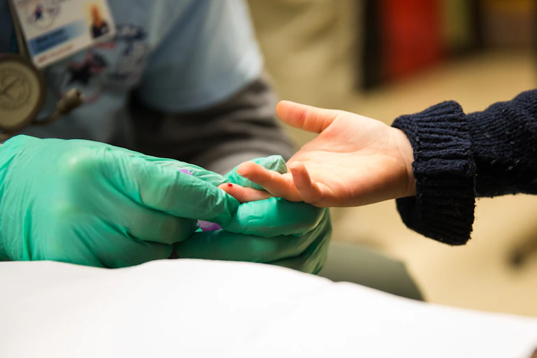A doctor takes a drop of blood from a child's fingertip.