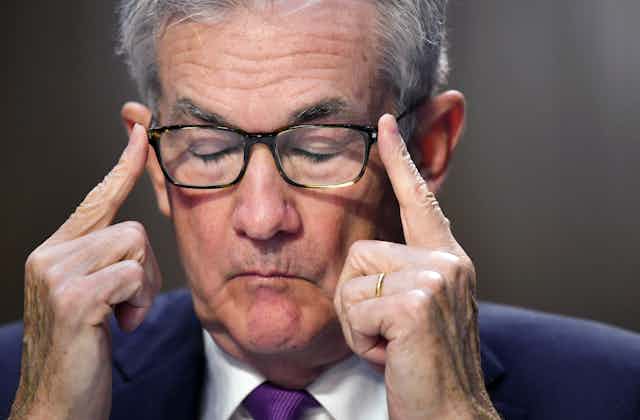Jerome Powell presses his forefingers on the ends of his eyeglasses with closed eyes