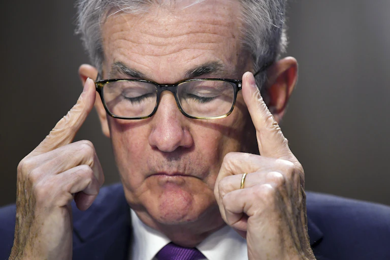 Jerome Powell presses his forefingers on the ends of his eyeglasses with closed eyes