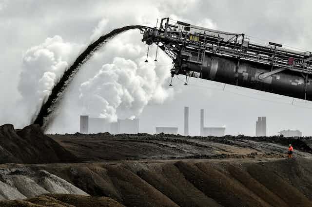 A large metal coal extractor spews a stream of coal onto a stockpile.