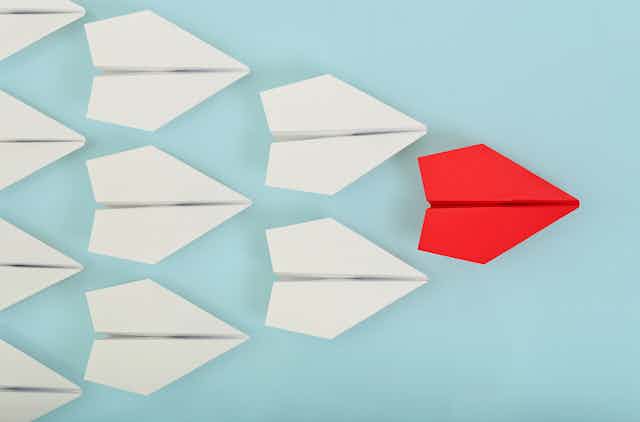 Nine paper planes on a pale blue background with one red paper plane out front symbolising the leader.