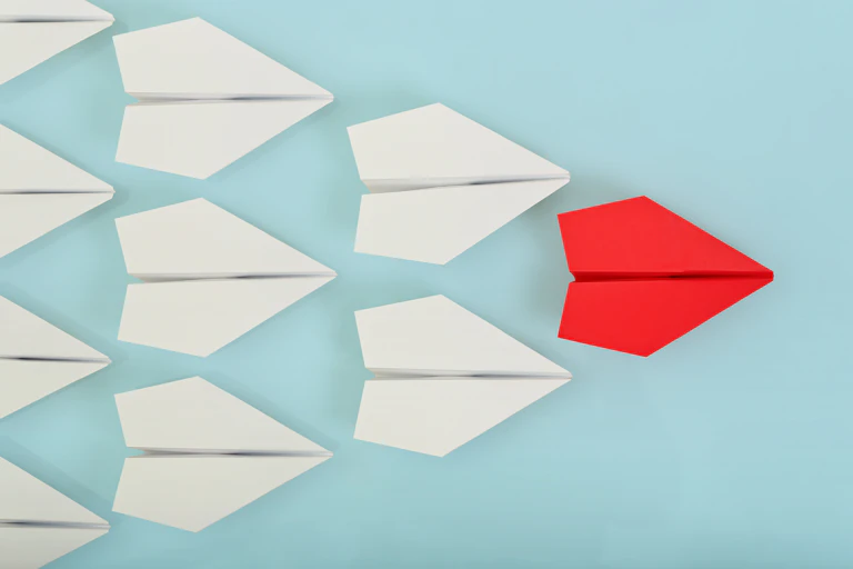 Nine paper planes on a pale blue background with one red paper plane out front symbolising the leader.