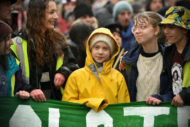 Greta Thunberg entourée de jeunes filles, tenant une banderole