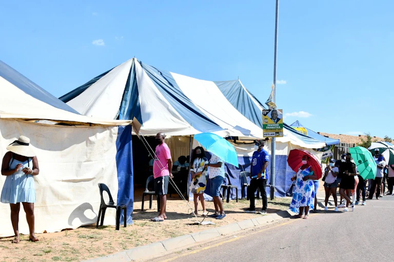 People line up along the road outside blue and white tents