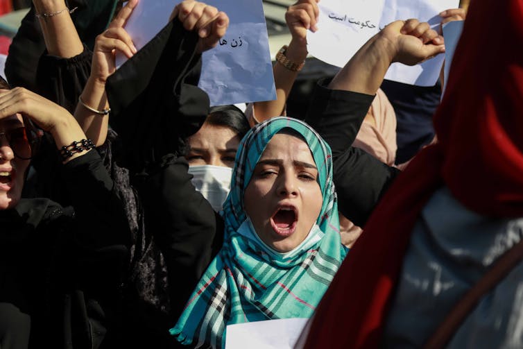 Women wearing hijab raise their fists and hold signs in protest.