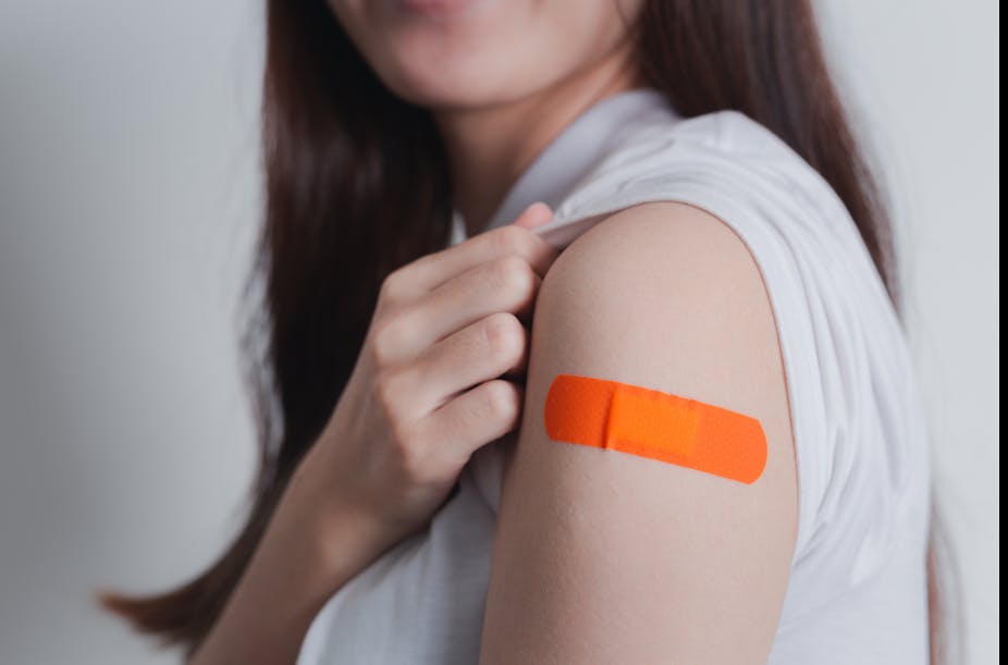 A young women shows off an orange bandaid on her arm after receiving a vaccine.