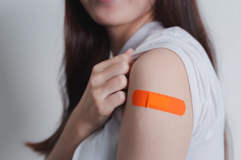 A young women shows off an orange bandaid on her arm after receiving a vaccine.