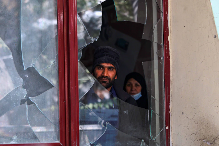 Man and woman stare outside of broken window.