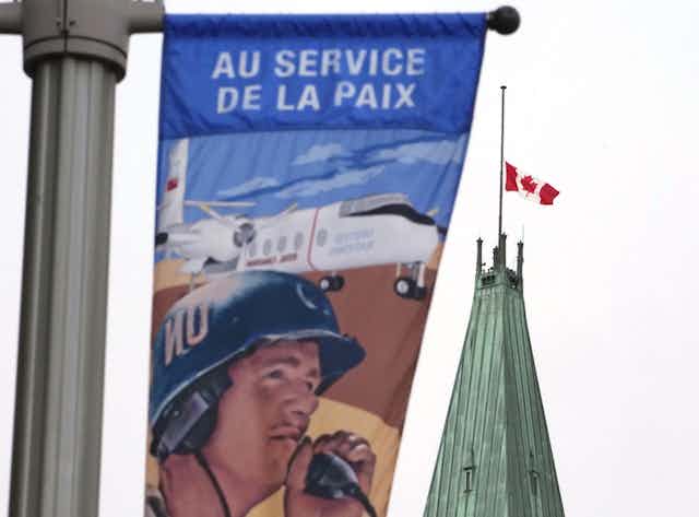 Canadian flag seen behind a banner about Canada's military that says ' au service de la paix'