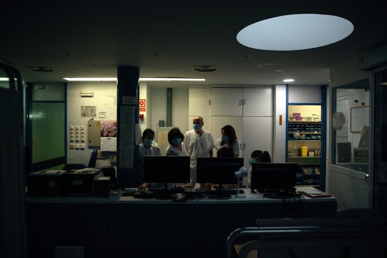 Health care workers crowded the ICU nursing station at night.