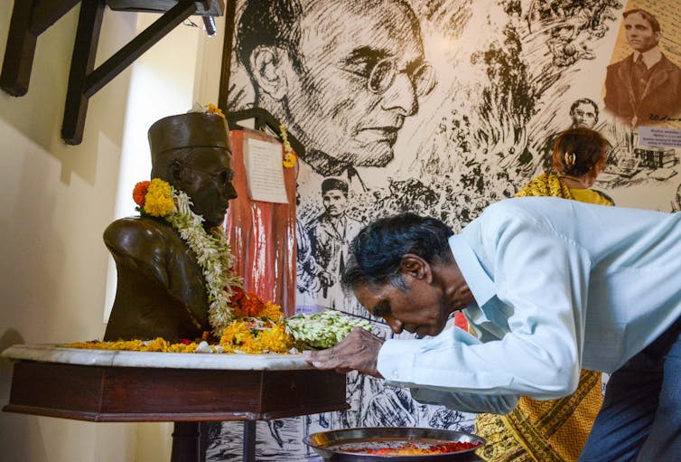 a man bows before a statue and a mural of a man.