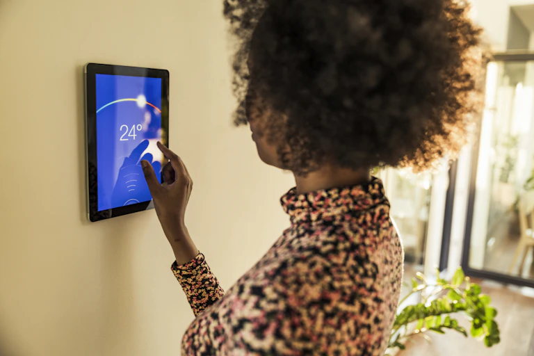 A woman adjusts the temperature on a smart thermostat set at 24C (75F).