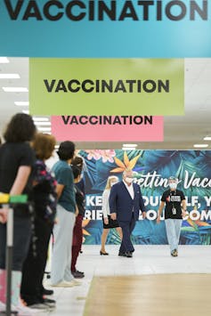 A vaccination centre with Ontario Premier Doug Ford in the background touring the facility and a line of people waiting to greet him in the foreground