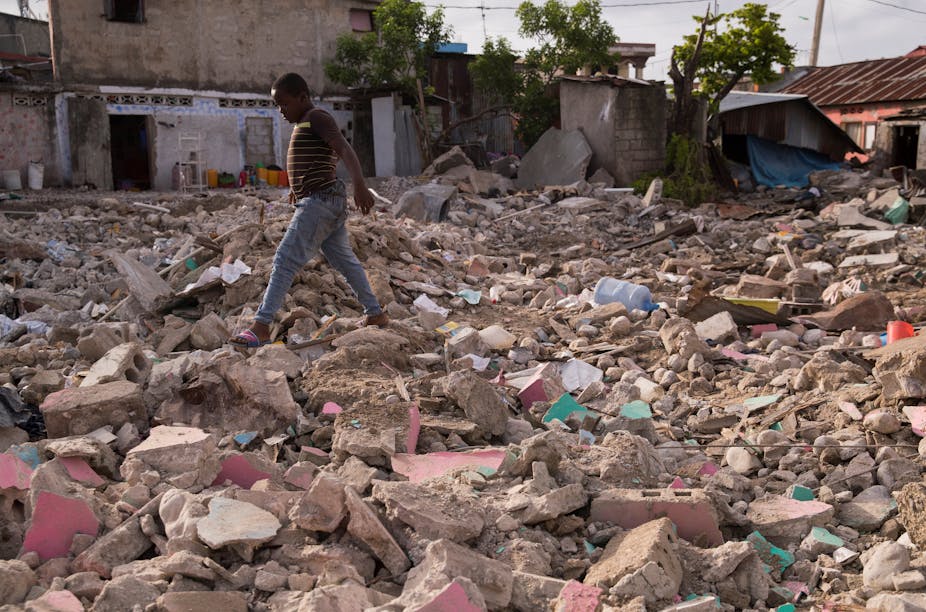 A boy walks across rubble of a destroyed house.