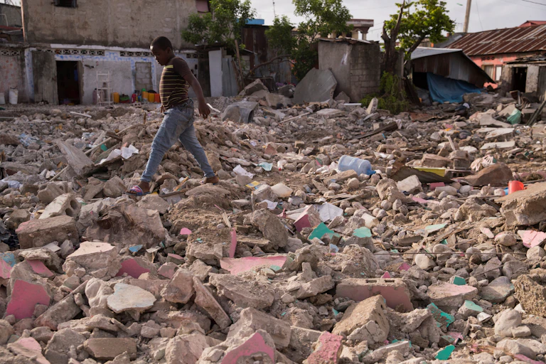 A boy walks across rubble of a destroyed house.