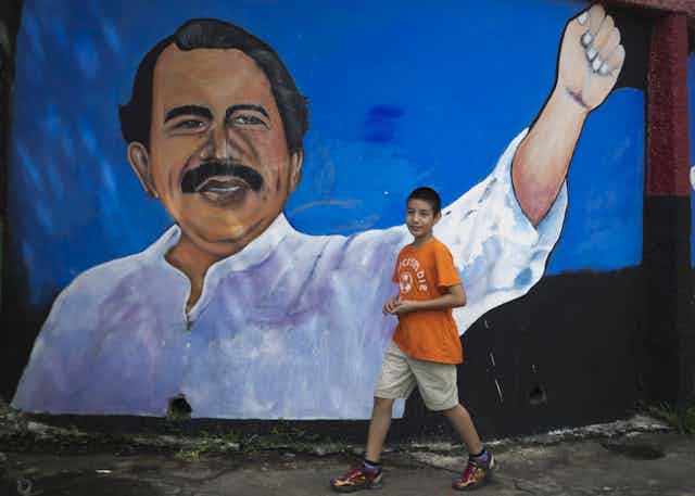 Young boy walks past mural depicting Nicaraguan leader Daniel Ortega.