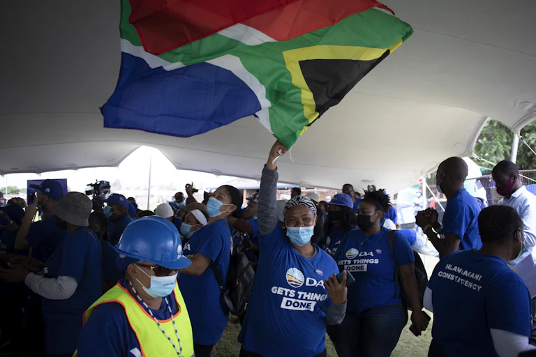 A woman wearing a COVID-19 mask and Democratic Allliance regalia waves the South African flag at a party election campaign meeting