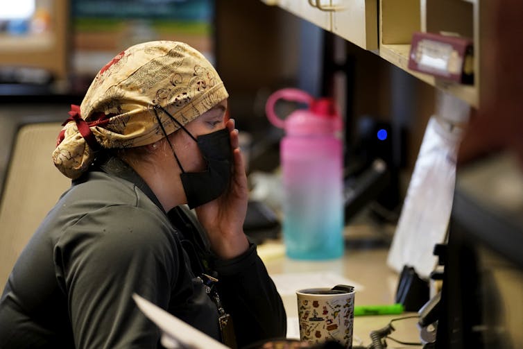 ICU nurse at computer with hand over their masked face.