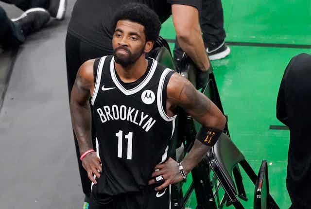 Kyrie Irving, wearing his Brooklyn Net jersey with number 11 written on it, rests his hands on his was it looks up at the fans at TD Garden after they defeated the Boston Celtics