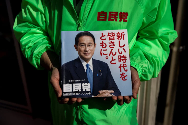 Un homme en imperméable vert tient un prospectus à l'effigie de Kishida Fumio